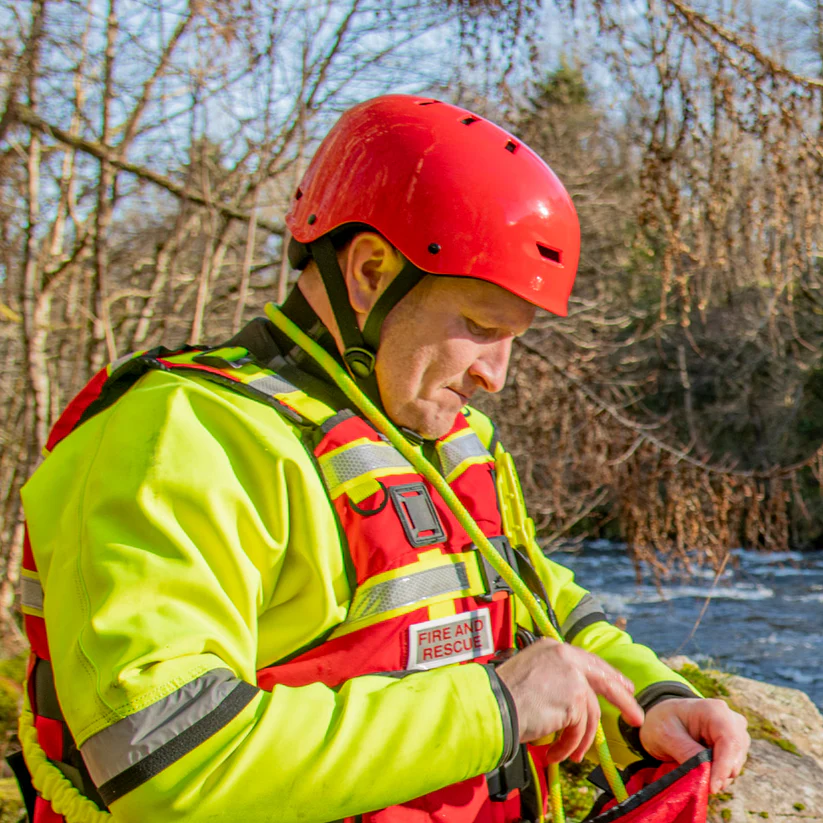 Einsatzkraft der Wasserrettung mit rotem Rettungshelm und Schwimmweste am Flussufer bei einer Strömungsrettungsübung – professioneller Schutzhelm für Feuerwehr, DLRG, Wasserwacht und Rettungsdienste.